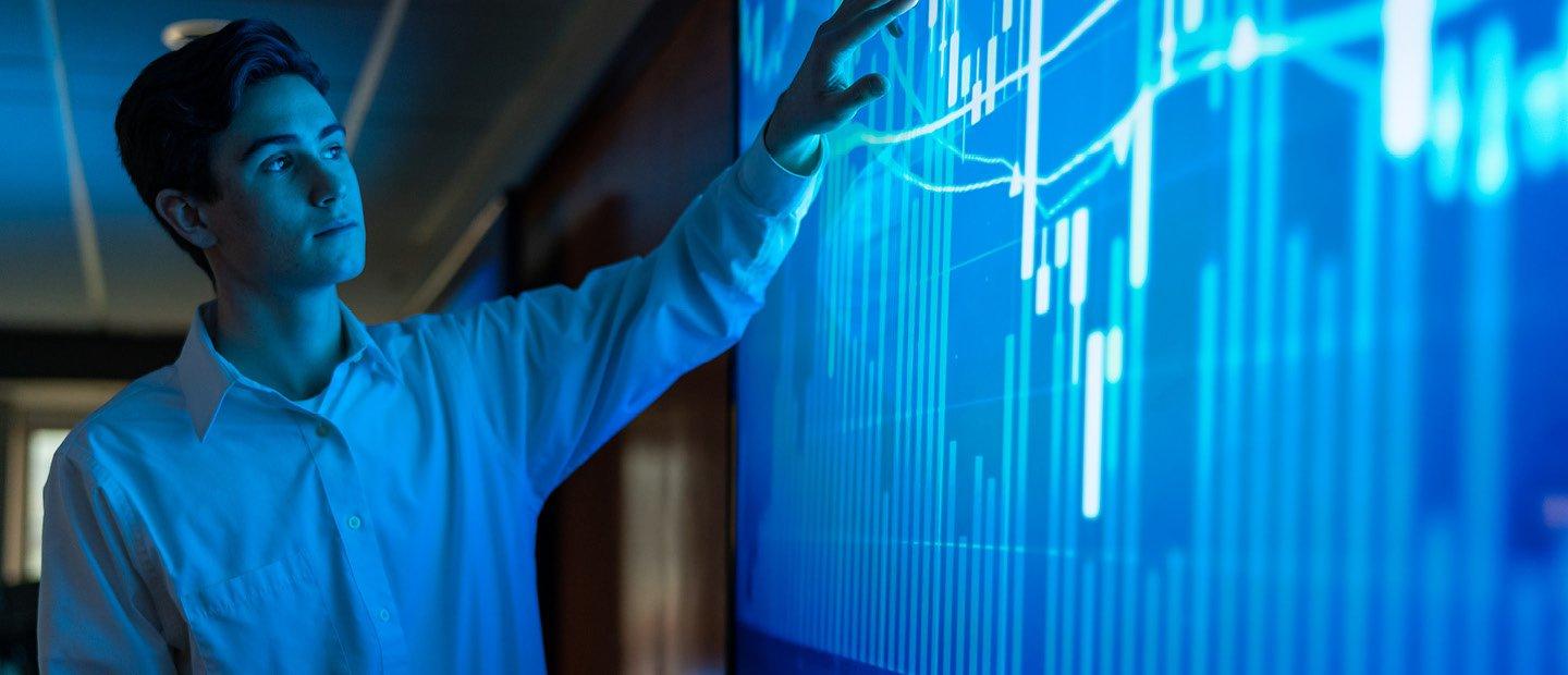 A young man pointing at a blue screen with a bar graph on it.